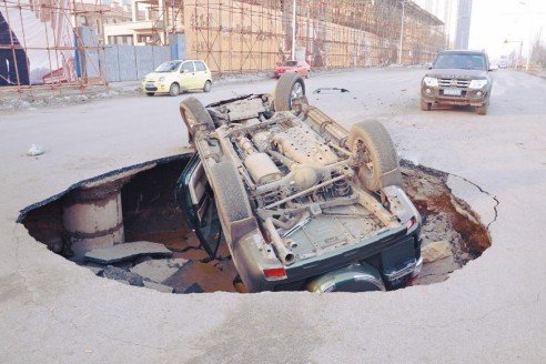 沈陽(yáng)一道路現(xiàn)大坑 霸道車遭橫禍四腳朝天(圖)